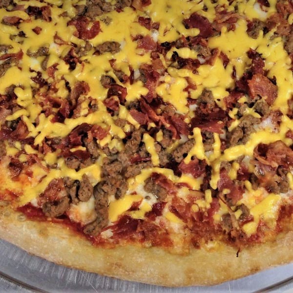 Close-up of a pizza with melted yellow cheese, ground meat, and bacon bits.