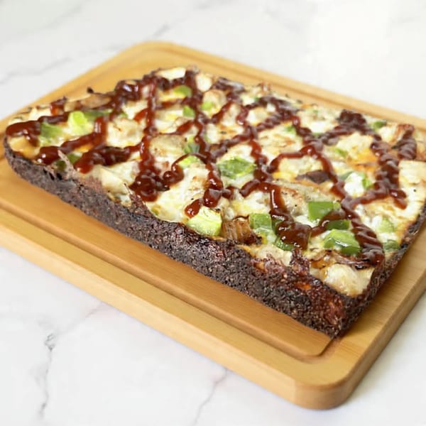 Rectangular Italian Village Pizza with BBQ sauce, chicken, and green peppers on a wooden board.