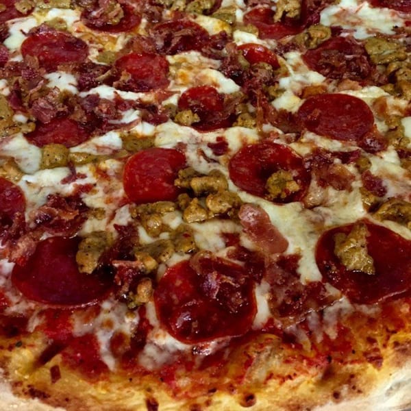Close-up of a meat lover's pizza from Italian Village Pizza, topped with pepperoni, sausage, and bacon.