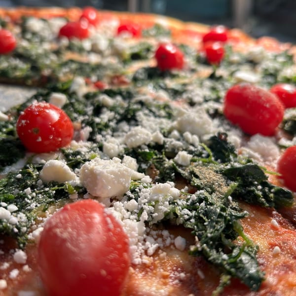 Close-up of a pizza topped with bright red cherry tomatoes, green spinach, and crumbled white cheese.