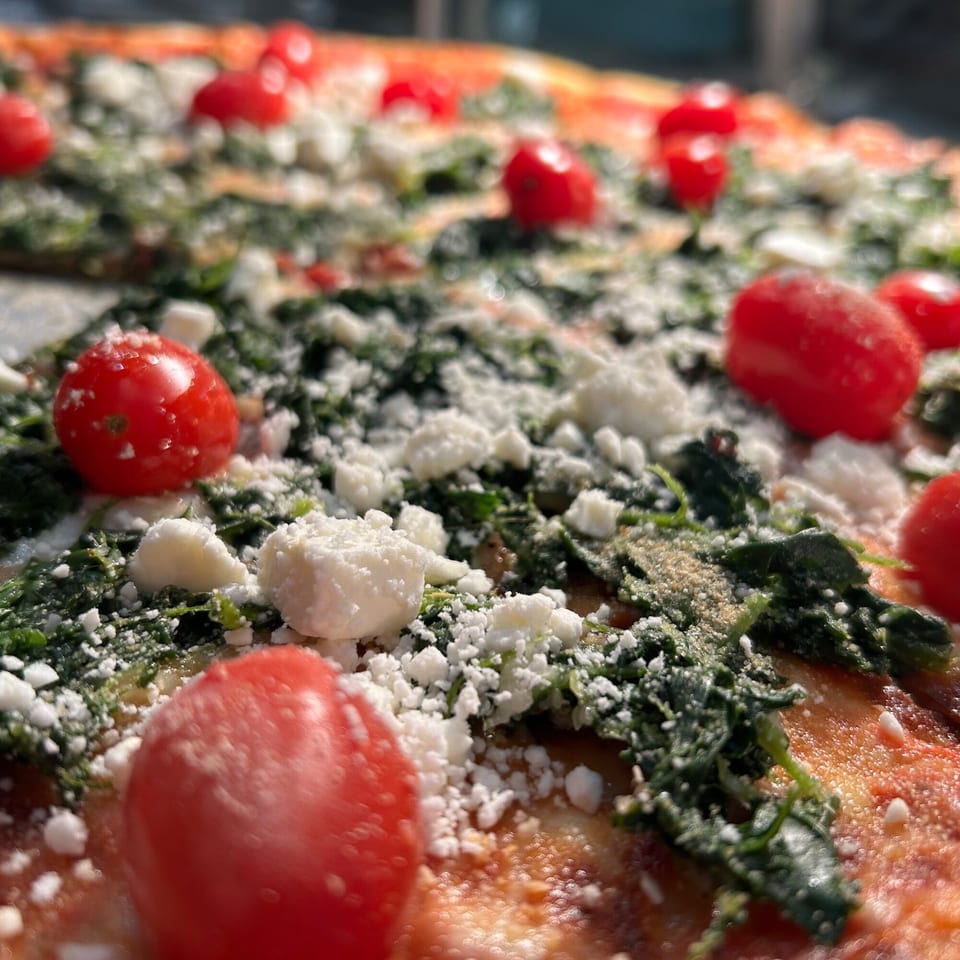 Close-up of a pizza topped with bright red cherry tomatoes, green spinach, and crumbled white cheese.