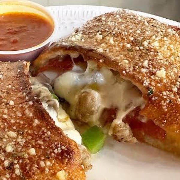 A golden-brown calzone, cut open to reveal melted cheese and fillings, with a side of marinara sauce.