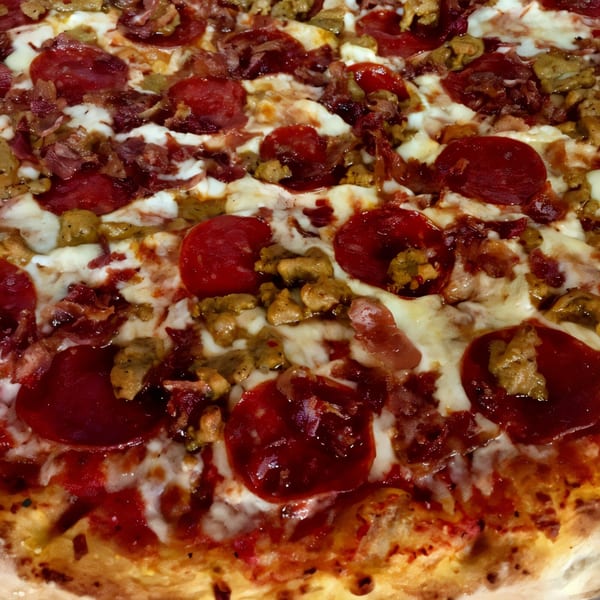 Close-up of a meat lover's pizza from Italian Village Pizza, topped with pepperoni, sausage, and bacon.
