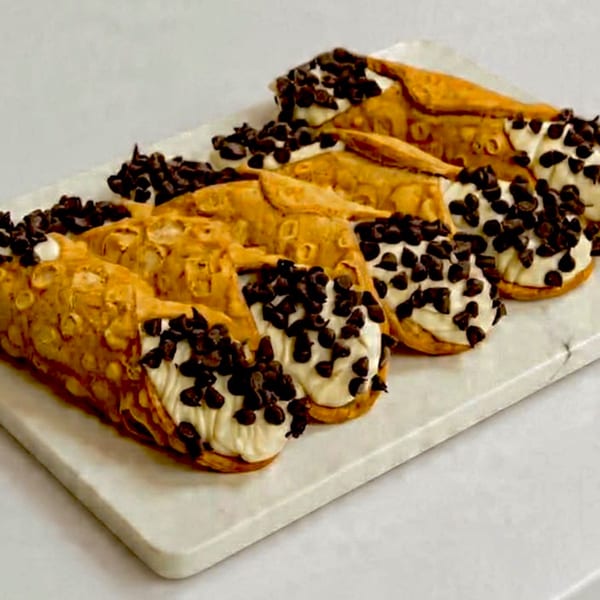 A white platter holds several Italian cannolis filled with cream and topped with chocolate chips.