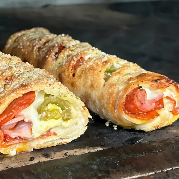 Two Italian Village Pizza strombolis, one sliced open revealing ham, pepperoni, cheese, and peppers.
